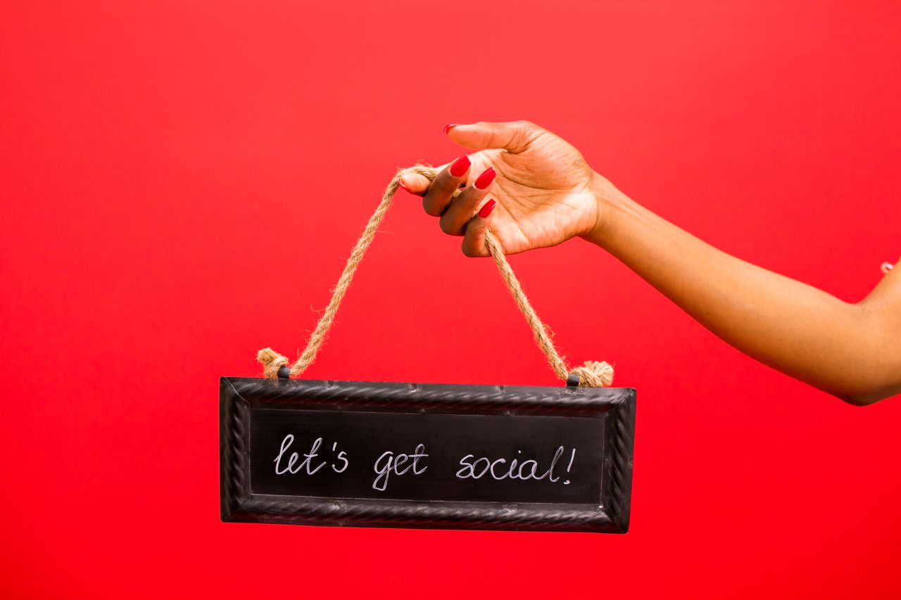 hero-img-01 A hand holding a 'Let's Get Social!' sign against a vibrant red background, perfect for online engagement themes.