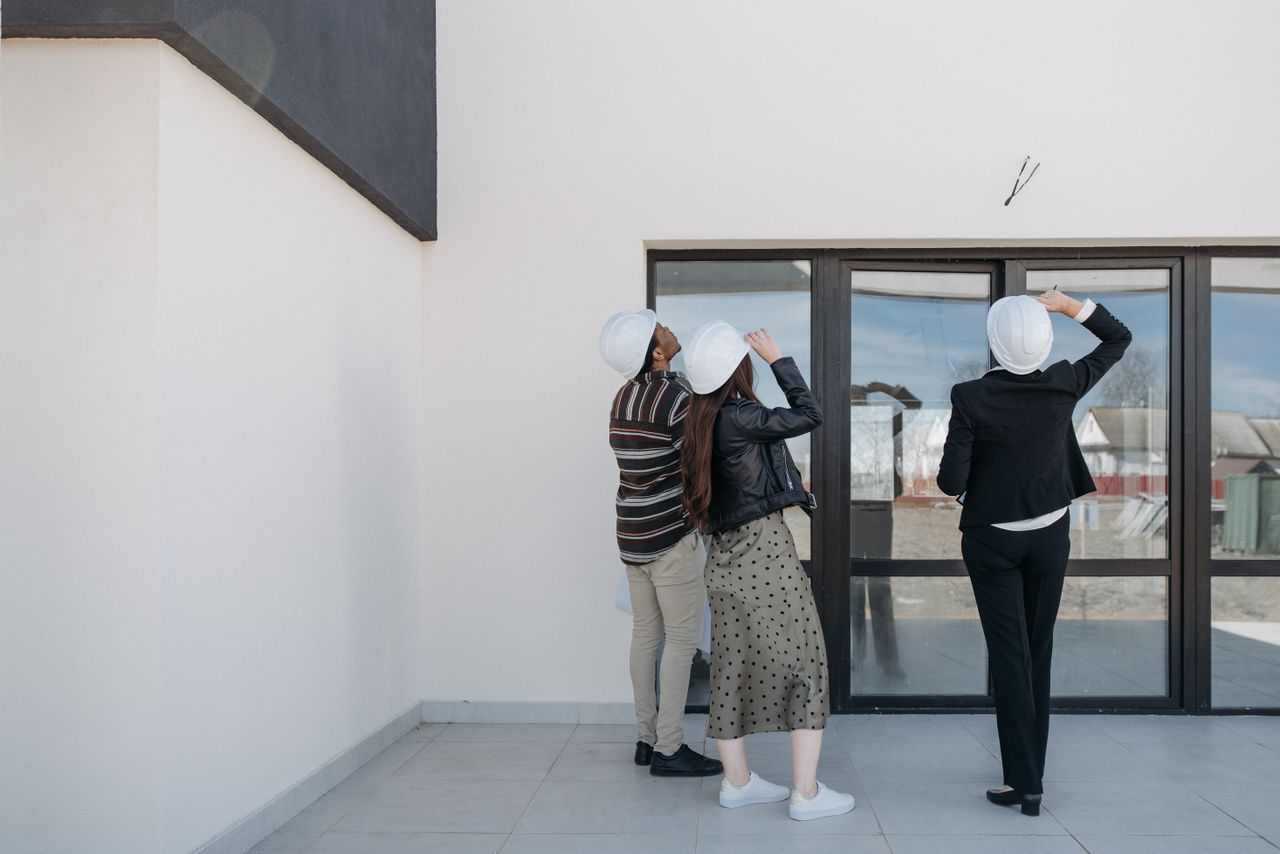 gallery-2 Three architects evaluating exterior building structure, wearing helmets and business attire.