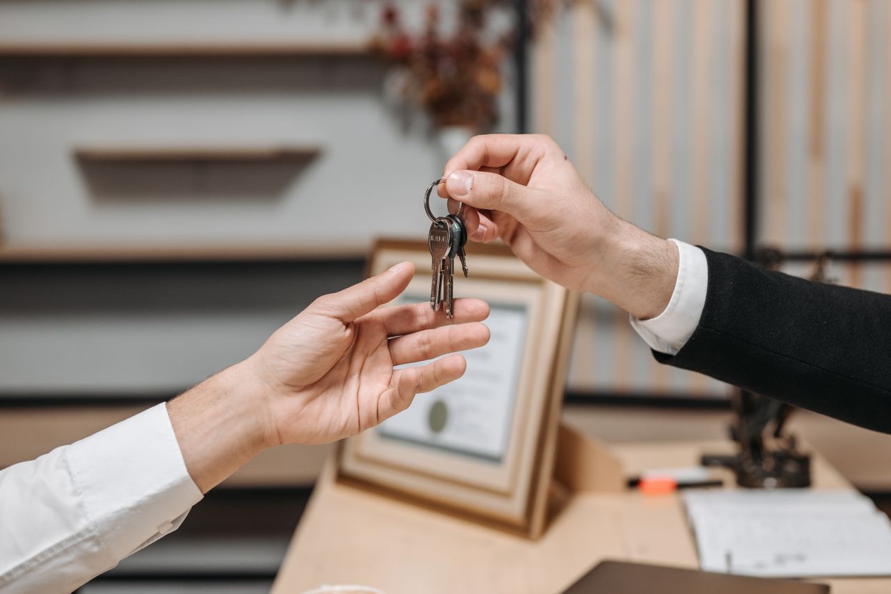 about-01 Detailed view of hands exchanging keys in a professional office environment, symbolizing real estate or business transactions.